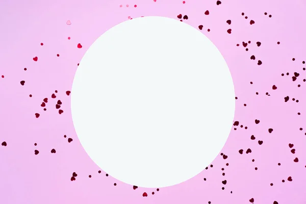 Mother\'s Day decoration concept. A picture of a white empty circle and sparkling heart-shaped sprinkles on an isolated pastel-pink background.