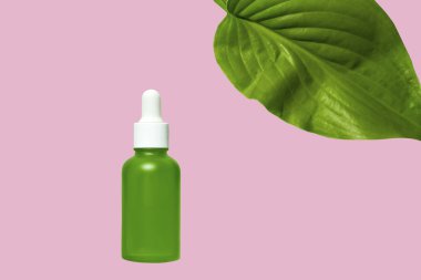 Pembe arka planda kozmetik ürünü olan yeşil cam damlası şişesi. Düz konum, üst görünüm, kopyalama alanı.