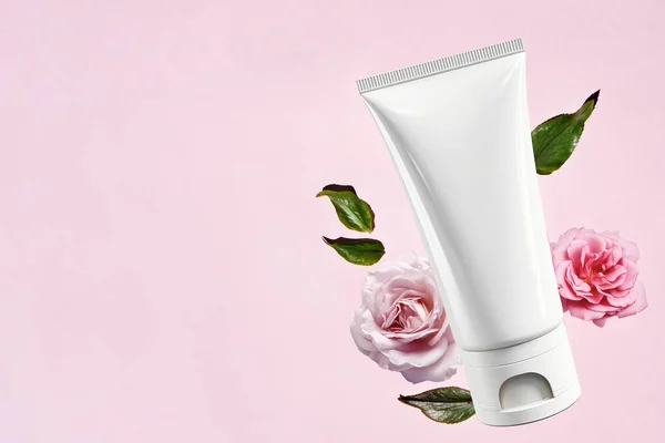 Biała Pusta Tuba Kosmetyczna Różowym Tle Delikatnymi Różowymi Różami Kosmetyki — Zdjęcie stockowe