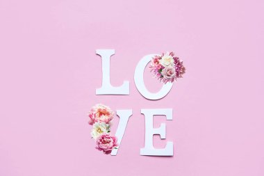 Kağıt harflerden ve pembe arka plandaki doğal çiçeklerden oluşan aşk kelimesi. Düzen düz, metin için boşluk var. Romantik arkaplan.