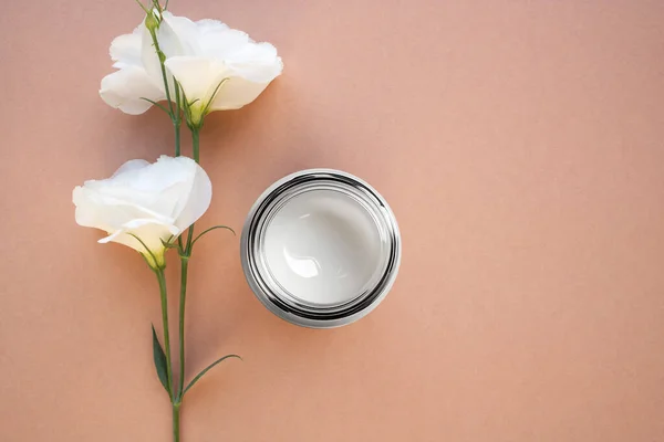 stock image A jar of moisturizing cream and a natural flower on a beige background. Top view, place for text.