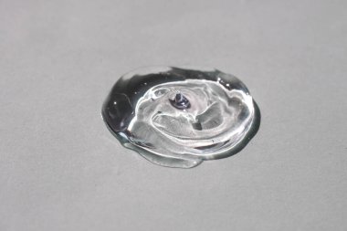 Gri arka planda bir damla berrak kozmetik jel.