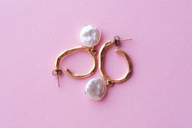 Açık pembe arka planda büyük incileri olan zarif küpeler. Üst görünüm.