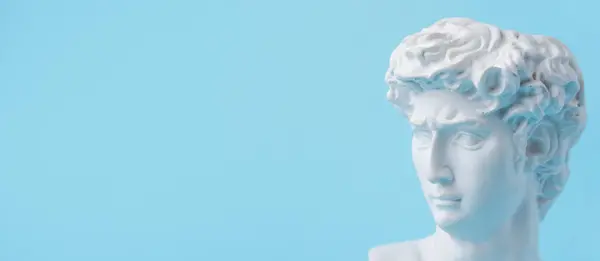 White plaster statue of David\'s head on pastel blue background. Minimalistic banner with space for text.