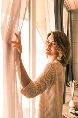 Pencerenin kenarında genç ve güzel bir sarışın duruyor.