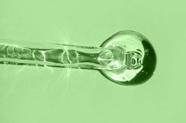 Aloe vera jeli bir damlatıcının yakın plan görüntüsü, canlı yeşil bir arka plan üzerine kurulmuş..