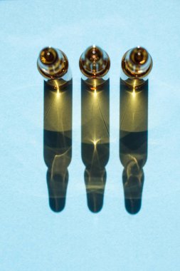 Arka arkaya mavi bir arka planda kozmetik ya da tıbbi ampuller. Ampullerin gölgesi var..