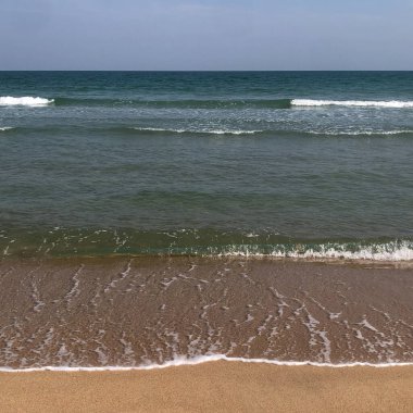Plaj dalgaları yaz gökyüzünün altında kumlu sahil boyunca yavaşça yuvarlanarak bu tropikal cennette sakin bir deniz manzarası yaratır.