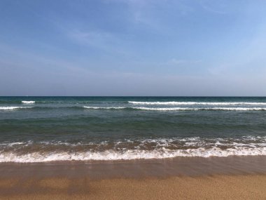 Plaj dalgaları yaz gökyüzünün altında kumlu sahil boyunca yavaşça yuvarlanarak bu tropikal cennette sakin bir deniz manzarası yaratır.