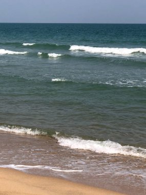 Plaj dalgaları yaz gökyüzünün altında kumlu sahil boyunca yavaşça yuvarlanarak bu tropikal cennette sakin bir deniz manzarası yaratır.