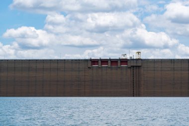 Kırmızı kapılı büyük kahverengi bir duvar bir su kütlesinin yanında yer alır. Su sakin ve gökyüzü bulutlu.