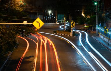 Uzun pozlama tekniği olan araba gece trafiğinde yola ateş ediyor. Kıvrımlı hareket yolları var. Karanlık yolda hızlı ışıklar var..