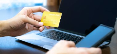 Kredi kartı tutan ve laptop ya da cep telefonu kullanan eller, online alışveriş, e-ticaret, internet bankacılığı, harcama parası, ev kavramından çalışma