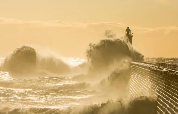 Big waves batter the lighthouse & north pier guarding the mouth of the Tyne in Tynemouth at sunrise, England