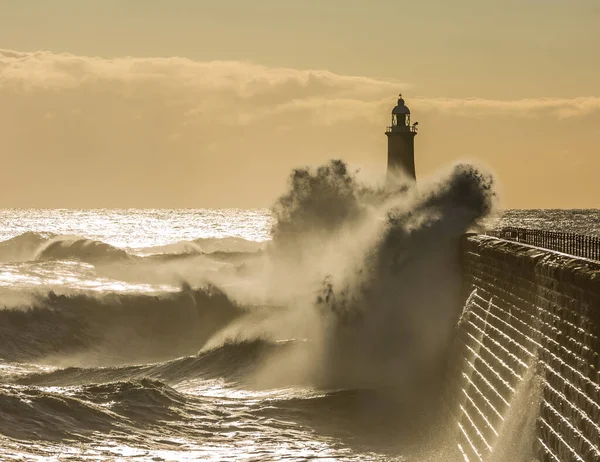 Big waves batter the lighthouse & north pier guarding the mouth of the Tyne in Tynemouth at sunrise, England