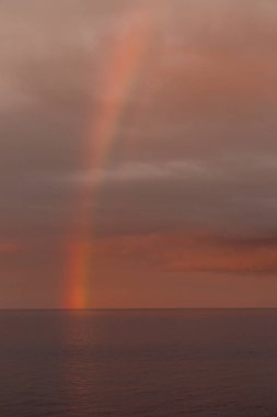 A dramatic sunset lights up the cloudy sky as a vibrant rainbow appears in Tynemouth in the North East of England clipart