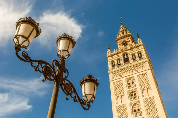 stock image La Giralda (translated to The Giralda), the bell tower of Seville's Cathedral next to the ornate old metallic streetlamps, Spain