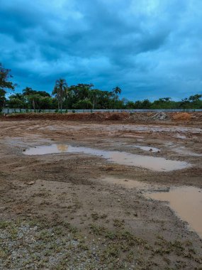 Durgun, çamurlu bir su birikintisi yağmurdan sonra çamura dönüşüyor. Gökyüzü koyu, ağır bulutlarla dolu..