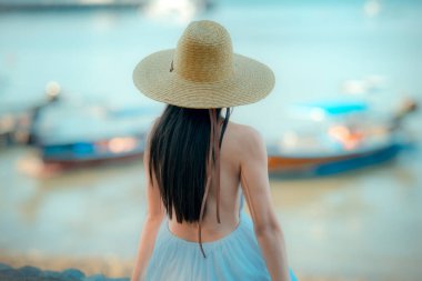 Kadın rahat bir şekilde oturur. Plajın kenarında rahatlar. Yaz tatilinde seyahat eder.