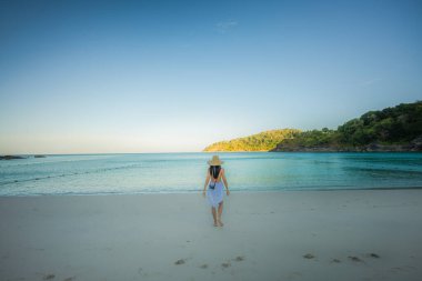 Giyinik kadın turist denizin kumsalında oynaşıyor, yaz kursunda deniz kıyısındaki kadının tadını çıkarıyor.