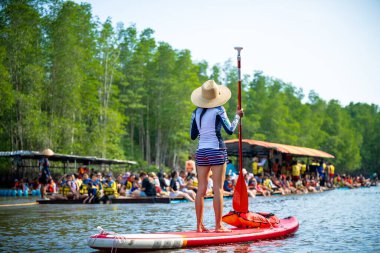 Kadın turistler yağmur ormanlarının doğal göl nehrinde stand-up sörfünün keyfini çıkarıyorlar. 