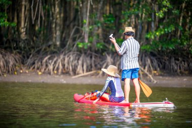 Çift turist, yağmur ormanlarının doğal göl nehrinde stand-up sörfünün keyfini çıkarıyor. 