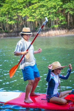 Çift turist, yağmur ormanlarının doğal göl nehrinde stand-up sörfünün keyfini çıkarıyor.
