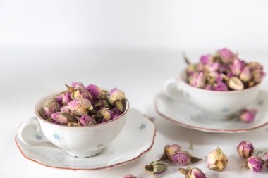 Beyaz porselen çay fincanı ve çay tabağında kurumuş gül tomurcukları.