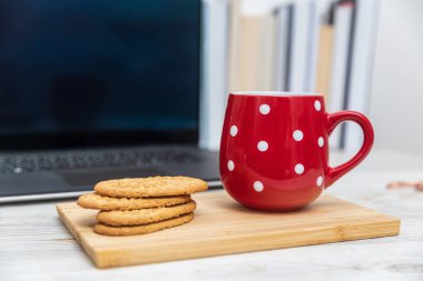 Tahta bir tahtanın üzerinde puantiyeli kırmızı bardak ve mısır gevreği. Arka planda bulanık bilgisayar ve kitap yığını