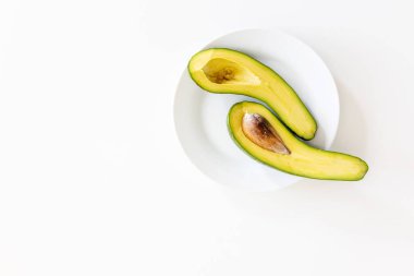 Avokadoyu beyaz bir masada bir tabakta ikiye bölün. Metin için yer