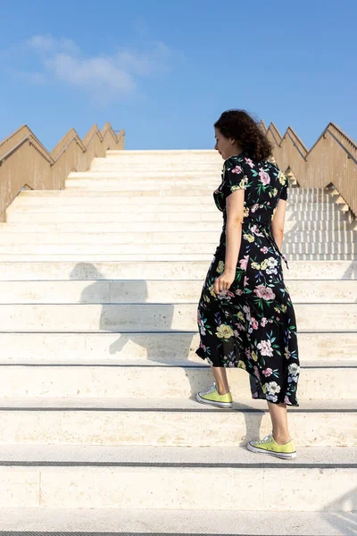 一个身穿黄花黑色连衣裙的20岁女孩爬上大理石楼梯 — 图库照片