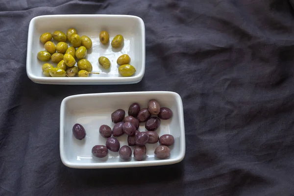 black olives and green olives in white saucers on a gray tablecloth on the table. Horizontal frame. Place for text