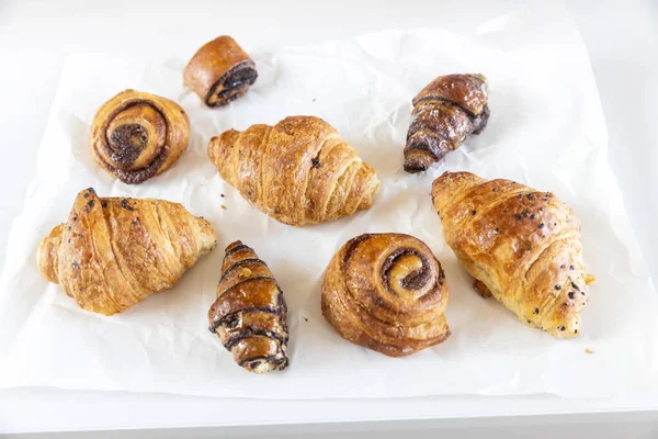 Fresh pastries - croissants with chocolate chips, poppy seed buns on a white sheet of paper on the table. Place for text
