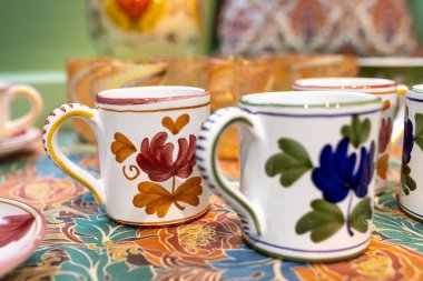 Mağazadaki bir rafta beyaz seramik tabaklar. Desenci seramik plakalar. Masa takımı ve yeme konsepti. Masa için güllü beyaz sürahi şarap için bardaklar ve su için bir şişe.