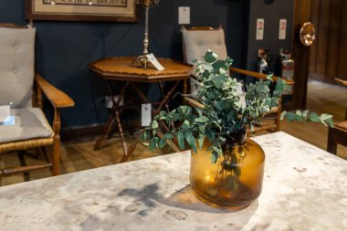 Londra, İngiltere - 10 Aralık 2022, bir buket yapay okaliptüs, içerideki küçük bir sehpanın üzerinde ağır sarı bir cam vazoda dallanır. Kış mevsimi trendleri. Özgürlük Lüksü Mağazası