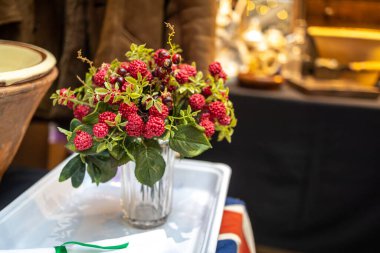 Masadaki vazoda kırmızı böğürtlen ve siyah frenk üzümü bulunan yapay dallar, çeşitli durumlar ve dekorasyonlar için.