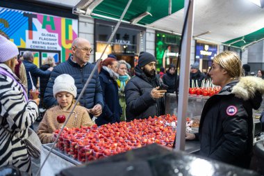 Londra, İngiltere - Aralık 2022, Kız kırmızı kremalı elmaları seçti. Covent Garden 'da çilek satan bir satıcı.