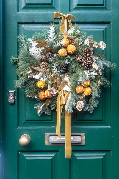 Christmas fir tree wreath decorated with artificial flowers and tangerine. Christmas wreaths on a green door in London
