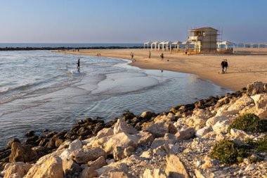 Haifa, Israel - January 20, 2023, Dado beach at sunset. People walk along the beach. Lifeguard booths.