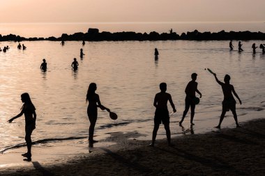 Tel Aviv İsrail - 07 Mart 2023, bir grup genç, Dado Sahili 'nde güneşin batışına karşı badminton oynuyor. Siluetler