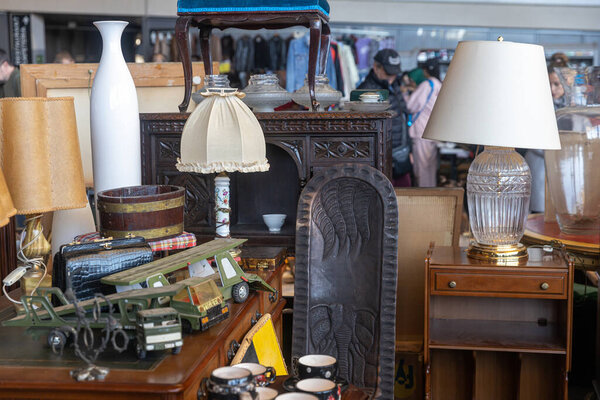 БАРСЕЛОНА - 14 марта 2023: Типичный киоск на блошином рынке Els Encants на площади Placa de les Gloriesa. Лампа с белой тряпкой абажура в стиле семидесятых годов и резной деревянной картиной