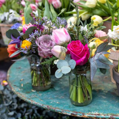 Kırmızı gül, okaliptüs, lale, ranunculus ve demir bir masada cam bir kavanozda mütevazı bir gelin buketi.