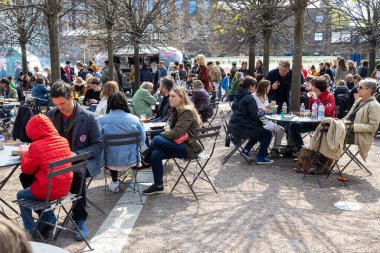 London UK - 15 Nisan 2023: Vintage 'dan Car Boot Sale. Retro festivali. İnsanlar klasik giysiler, mücevherler, klasik araçlarında ev eşyaları satıyorlar. İnsanlar kırmızı kafe otobüsünün yanında bira içiyorlar.