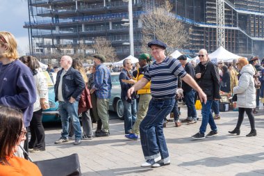 London UK - 15 Nisan 2023: Vintage 'dan Car Boot Sale. Retro festivali. İnsanlar klasik giysiler, mücevherler, klasik araçlarında ev eşyaları satıyorlar. Eski moda kot pantolonlu adam dans ediyor.