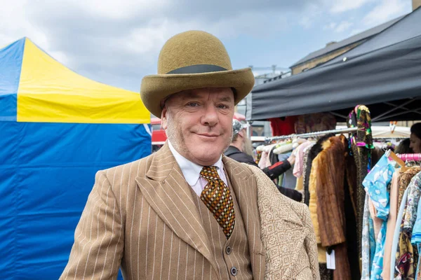 stock image London UK - April 15 2023: Car Boot Sale by Vintage. Retro festival. People sell vintage clothing, goods jewellery, homeware on classic vehicles. A man in a gray tweed suit and a tall hat with a cane.