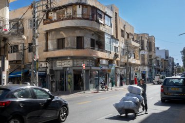 Tel Aviv, İsrail - Nisan 2023, bir adam çanta ve kutularla dolu bir arabayı itiyor. Yükleyici çalışıyor.