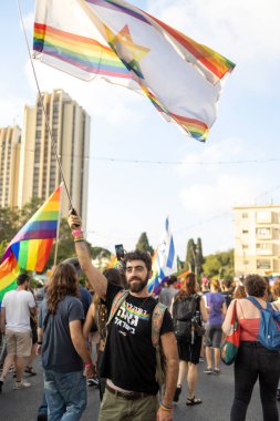 Hayfa, İsrail - 24 Haziran 2023: Geleneksel LGBTQ onur yürüyüşü için protesto tabelaları taşıyan insanlar. Adam gökkuşağı bayrağı sallıyor