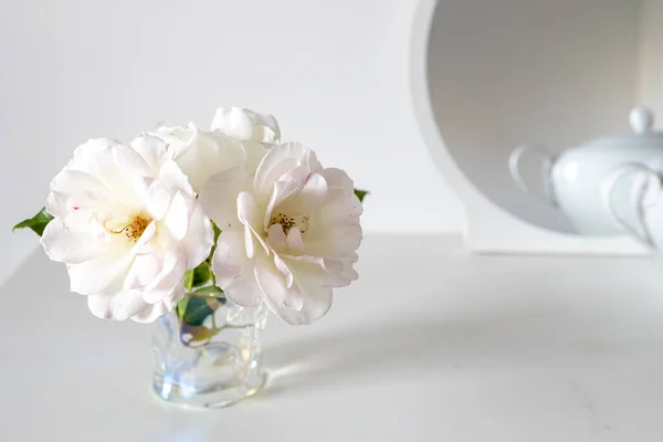 Tea white rose in a transparent glass on white table. Place for text.