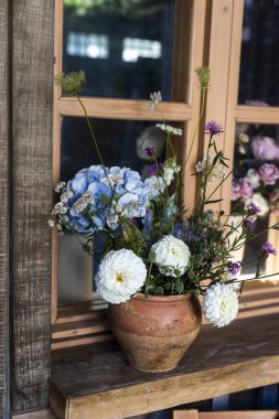 Kırsal bir buket mavi ortanca, beyaz kasımpatı ve yıldız çiçekleri, ve kahverengi bir şişe içinde hindiba ahşap bir masada verandanın süsü olarak.