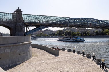 Moskova, Rusya - 15 Mayıs 2021: Puşkin setinin manzarası. İnsanlar nehrin kıyısında kütüğe oturur. Gemi köprünün altından geçiyor. Anne ve çocuk merdivenlerde durun. Gorky Kültür ve Eğlence Merkezi Parkı